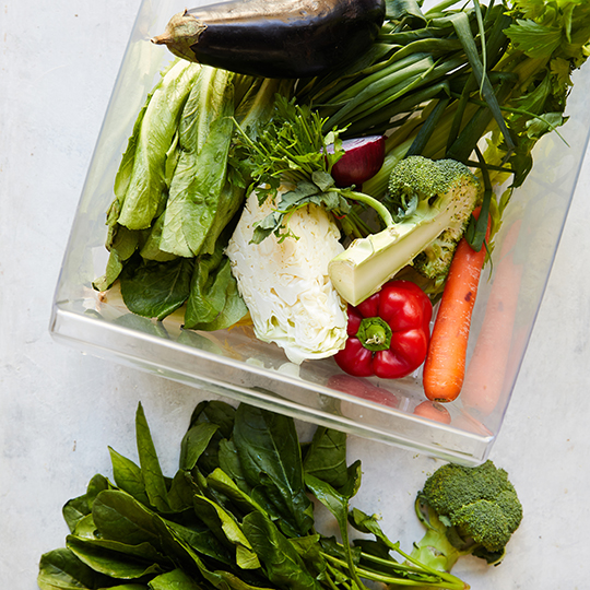 A variety of vegetables sitting in and alongside a fridge crisper